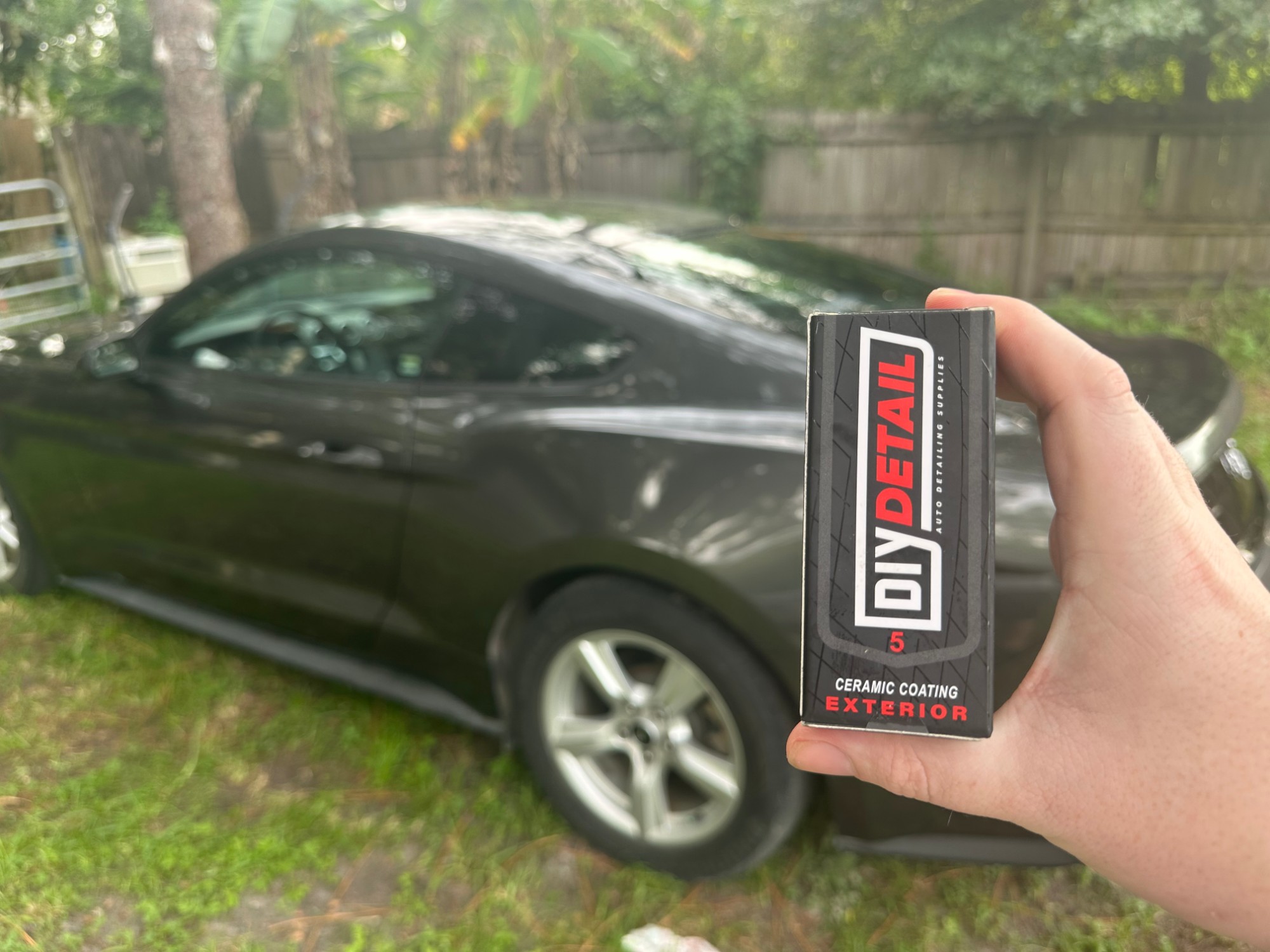 A boxed DIY ceramic coating kit held up next to a black Ford Mustang before a professional ceramic coating application in Lutz, FL